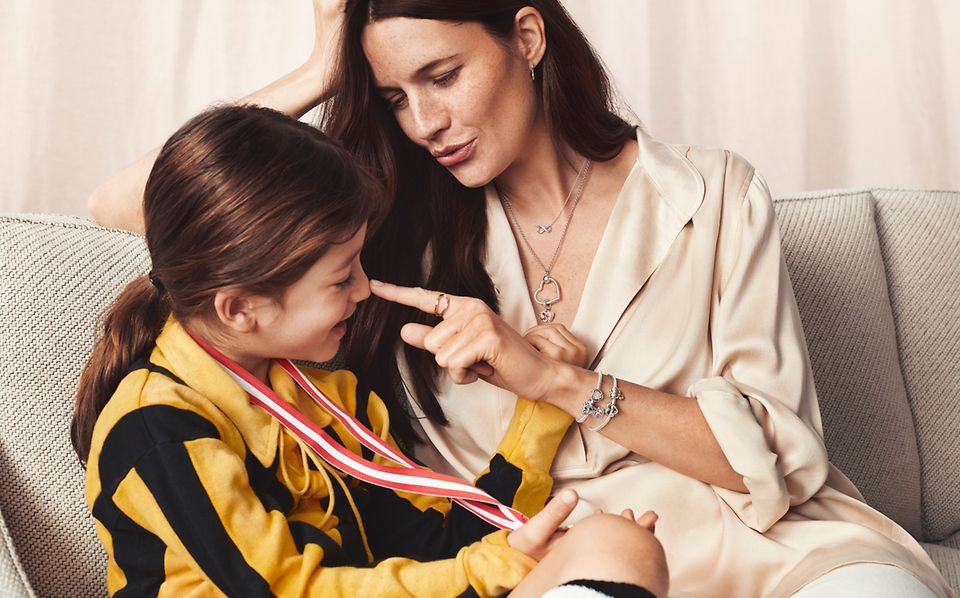 Madre seduta con la propria figlia che indossa un pendente Pandora O e bracciali con charm.