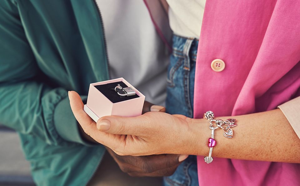 Main portant un bracelet avec des charms tenant une boîte à bijoux munie d'un charm