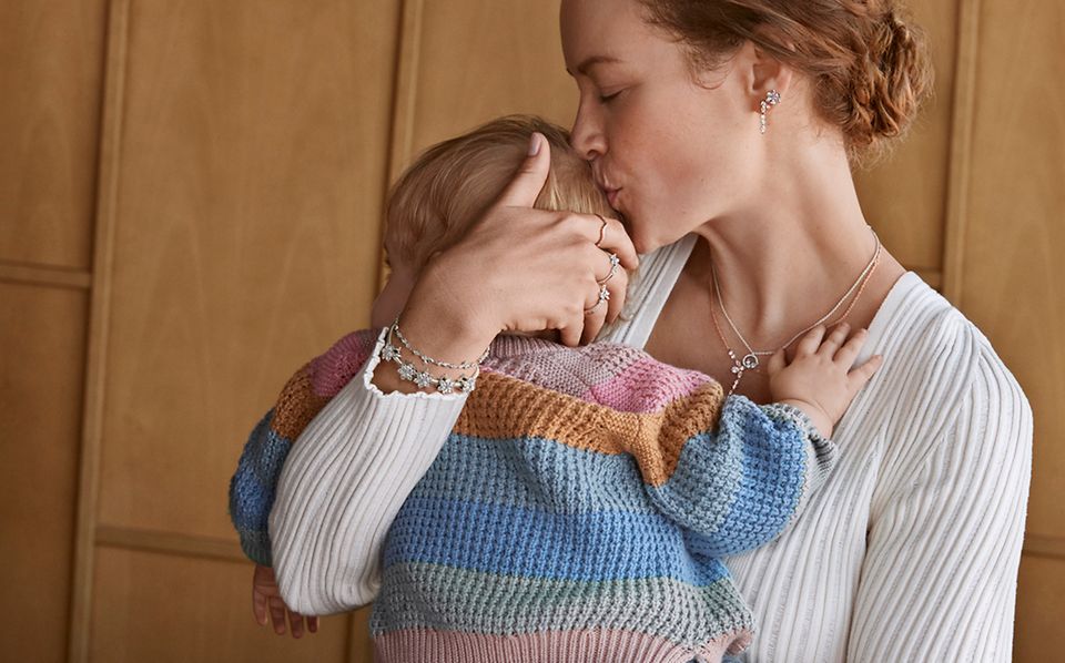 Mamma che indossa un gioiello Pandora per la Festa della Mamma e che coccola il suo bebè baciandone la testina