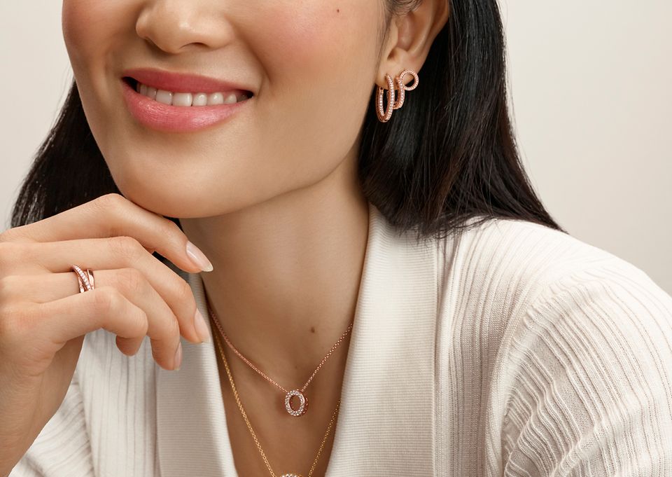 Close up of woman in white top wearing rose gold jewelry from Pandora Signature.