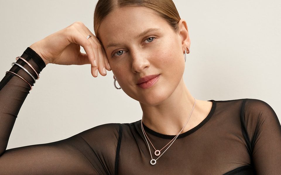 Woman in black dress sat wearing jewellery from Pandora’s Signature collection.