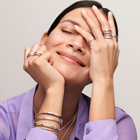 Kvinde i lilla skjorte, der bærer Pandora Signature stabelbare ringe og armbånd