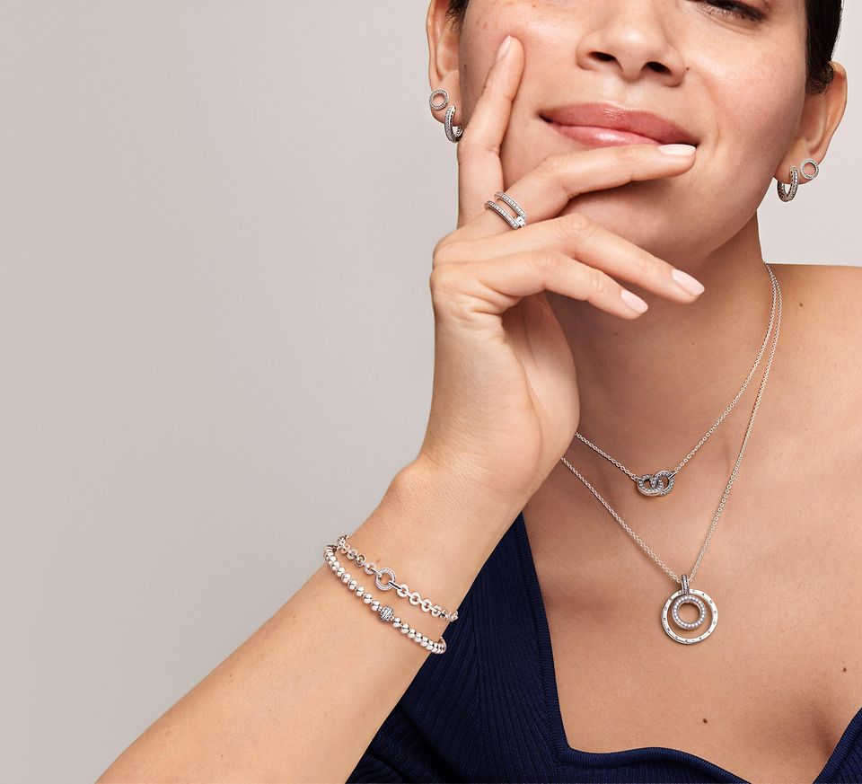 Kvinde, der bærer Pandora Signature stabelbare ringe, armbånd, øreringe og halskæder