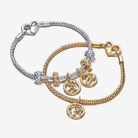 シルバーブレスレットの上に、ゴールドの Pandora Moments Zodiac Charm Bracelet を重ねづけした画像