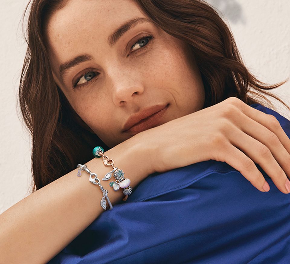 Kvinna i mörkblått som bär två Pandora Moments-berlockarmband