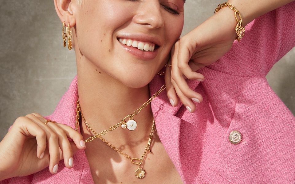 Woman smiling and wearing Pandora ME gold necklaces, earrings and a bracelet.