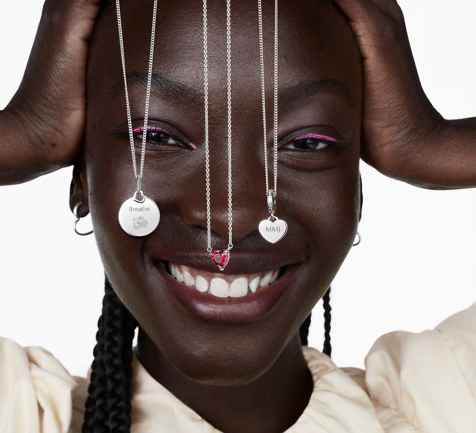 Lachende vrouw met drie zilveren Pandora-halskettingen die voor haar gezicht hangen