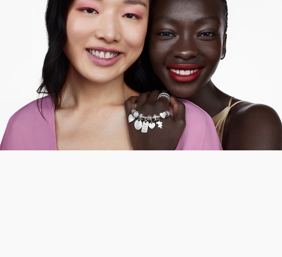 Zwei Frauen lächeln, eine trägt ein silbernes Pandora Armband, Ringe und Ohrringe 