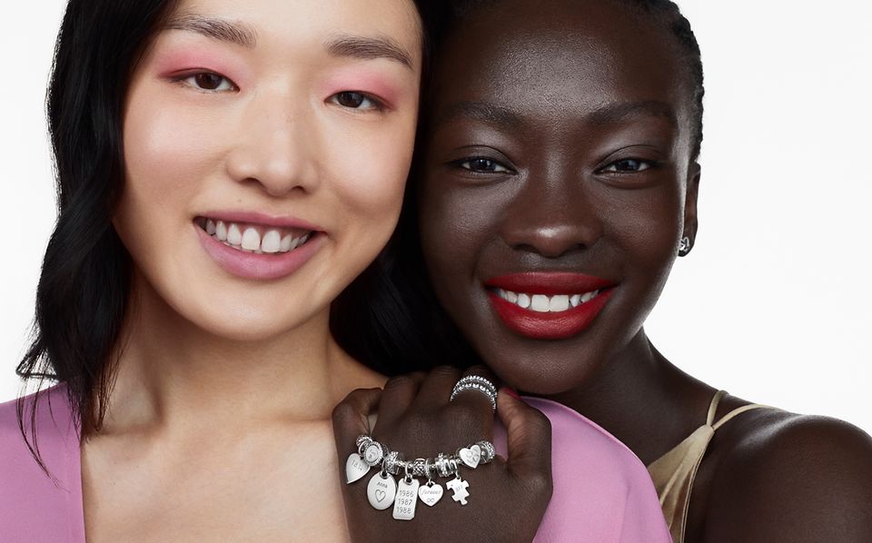 Dwie uśmiechnięte kobiety, jedna ma na sobie srebrną bransoletkę, pierścionki i kolczyki Pandora 