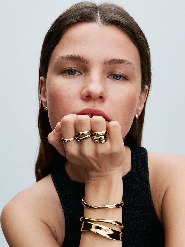 Modelka nosi złote bransoletki, pierścionki do łączenia i kolczyki z kolekcji Pandora Essence.